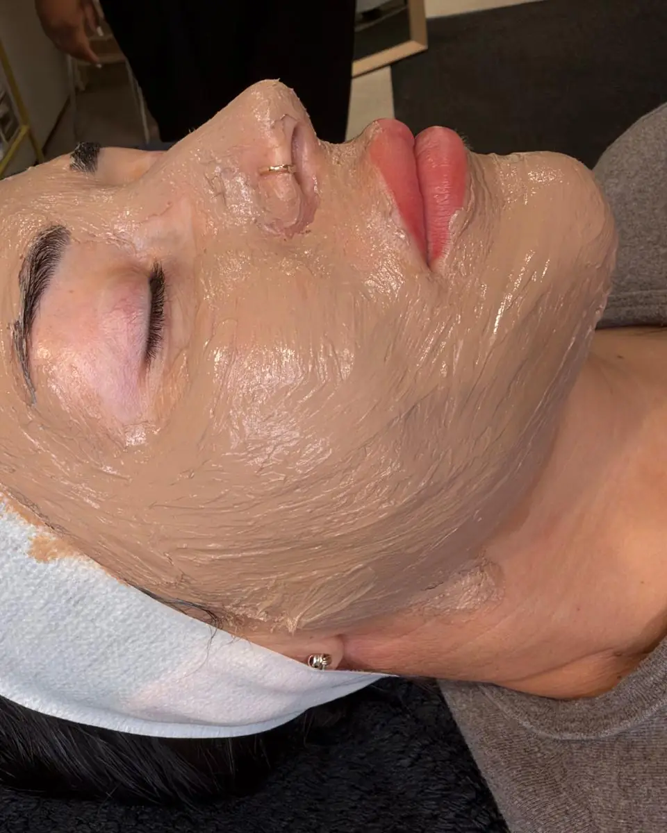 A client lying back in the Glow By Yaz treatment room wearing a tan-coloured professional peel mask, hair held back with a white headband