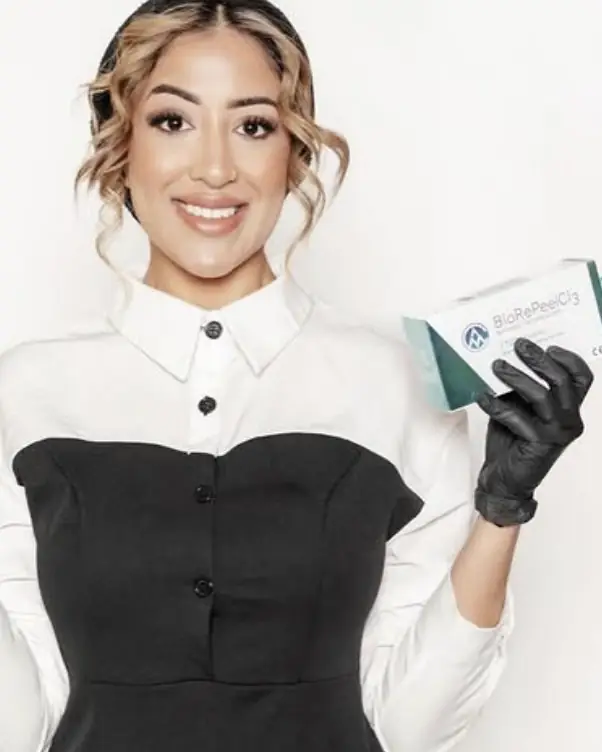 Yaz, founder of Glow By Yaz, smiling in a white collared shirt and black dress, holding a box of BioRePeel